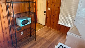 A room with wooden paneling, a white door, a white refrigerator, and a blue microwave on a black wire shelf. - Cozy 1-bedroom apartment in nice Brownwood with AC (Brownwood)