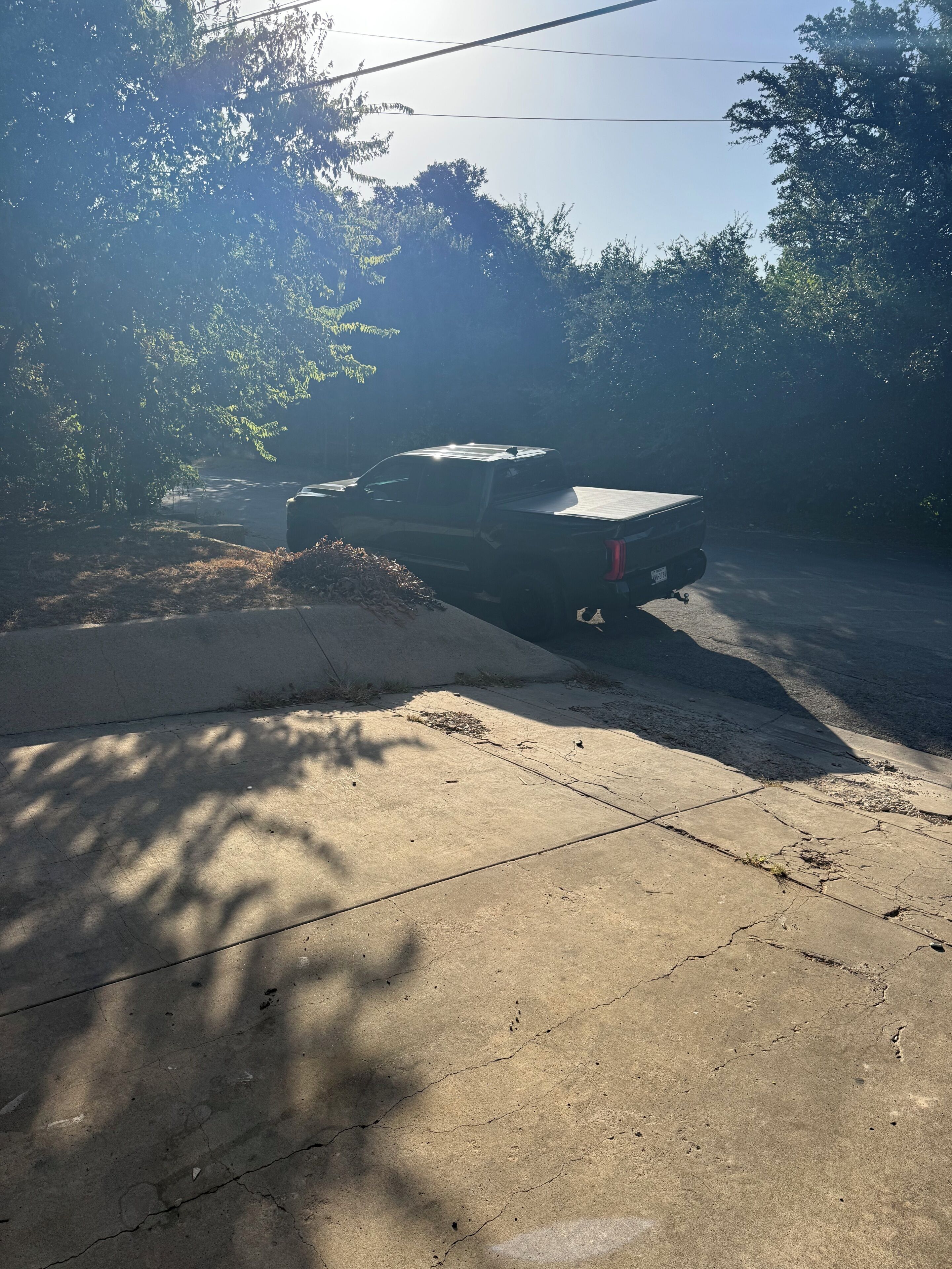 A parked vehicle on a concrete surface with shadows of trees.
