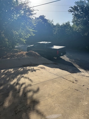 A parked vehicle on a concrete surface with shadows of trees.