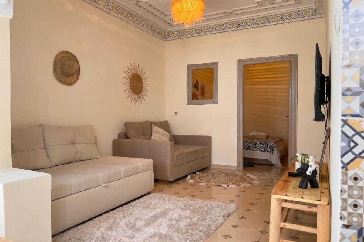Un salón con dos sofás, una mesa de centro, una alfombra, un adorno de sol, un televisor montado en la pared y un suelo con diseño.