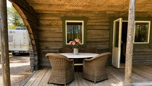 A wooden cabin with a porch, wicker chairs, a table, and a vase of flowers. - Cabin in the Woods (Malung)