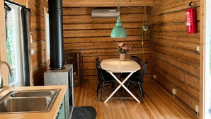 A wooden cabin interior with a kitchen, dining area, and a black chimney. - Cabin in the Woods (Malung)