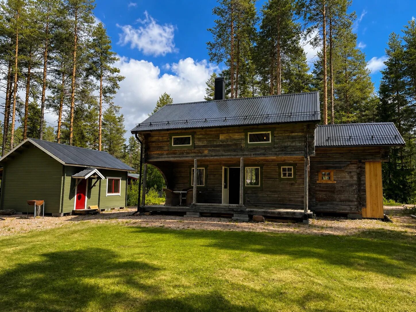 A rustic cabin with a metal roof, a wooden porch, and a small attached shed.