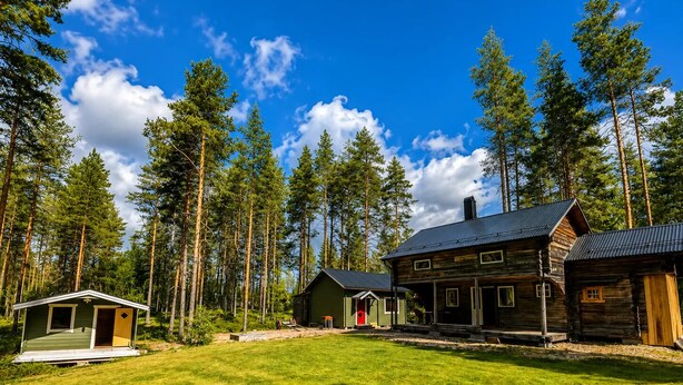 A cabin with a porch, a small shed, and a large wooden building with a chimney. - Cabin in the Woods (Malung)