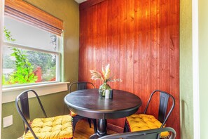 A dining area with a round table, two chairs, a vase with flowers, and a window with a view of greenery. - Relax & Recharge • King Bed Retreat • Sleeps 4 (Dallas)