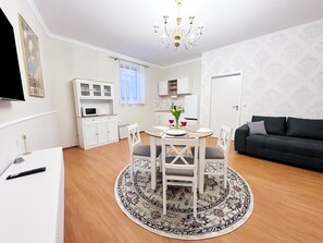A modern living room with a dining area, a black sofa, a chandelier, and a kitchen in the background. - Sophia Neighborhood - Spacious 92-square-meter basement apartment near Goethepark (Weimar)