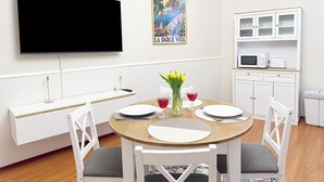 A dining area with a round table, white chairs, a TV mounted on the wall, a poster, and a kitchen area with cabinets and appliances. - Sophia Neighborhood - Spacious 92-square-meter basement apartment near Goethepark (Weimar)