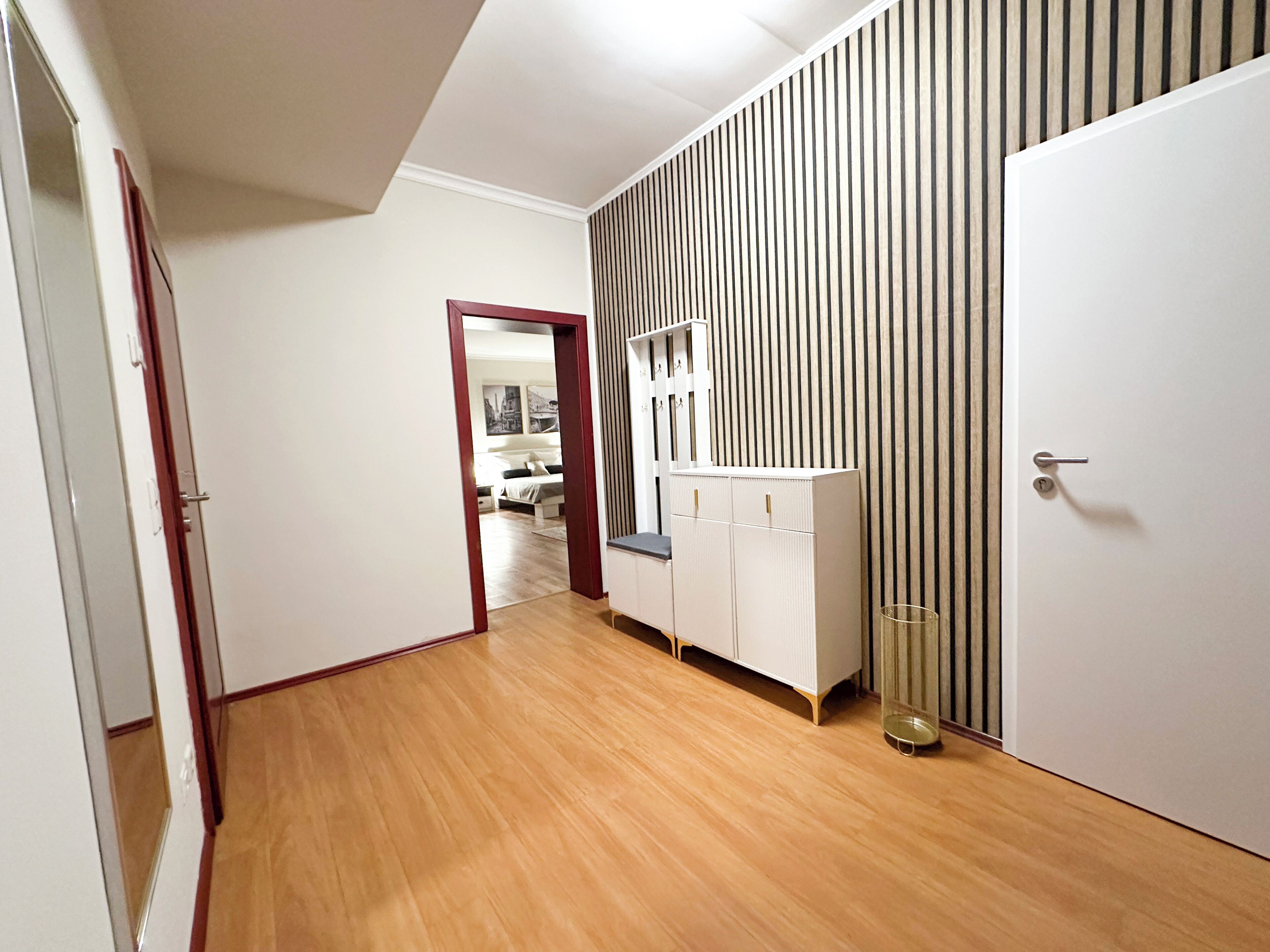 Ein Flur mit Holzboden, einem weißen Kleiderschrank und einer Spiegelklappe.