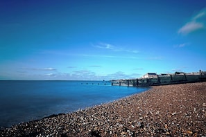 A pebble beach with a pier extending into calm waters, a clear sky, and a building on the right. - Beach Oasis | 2 Bedroom Flat & Free Parking (Kent)