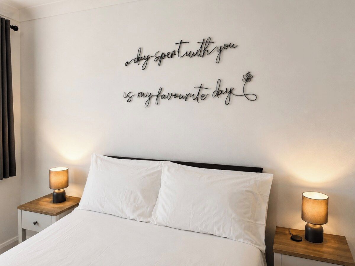 A hotel room with a bed, two bedside lamps, and a wall with a decorative sign.