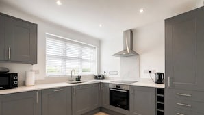 A modern kitchen with grey cabinets, a microwave, a kettle, and a window with blinds.