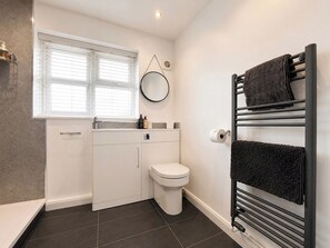 A modern bathroom with a toilet, a sink, a towel rack, and a window with blinds. - Beach Oasis | 2 Bedroom Flat & Free Parking (Kent)
