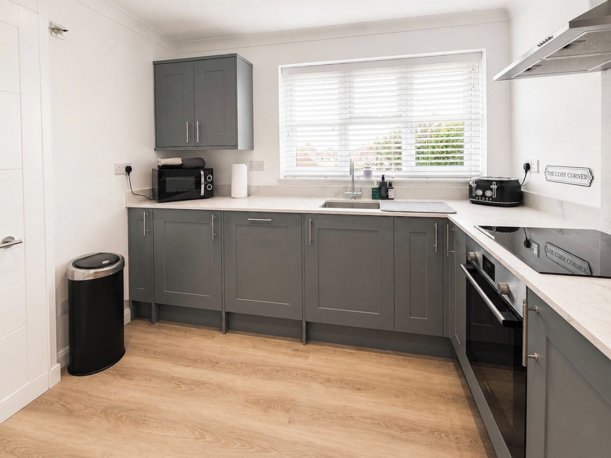 A modern kitchen with grey cabinets, a microwave, a sink, and a window with blinds.
