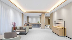 Un moderno vestíbulo de hotel con una recepción, zona de estar y un banco de madera.
