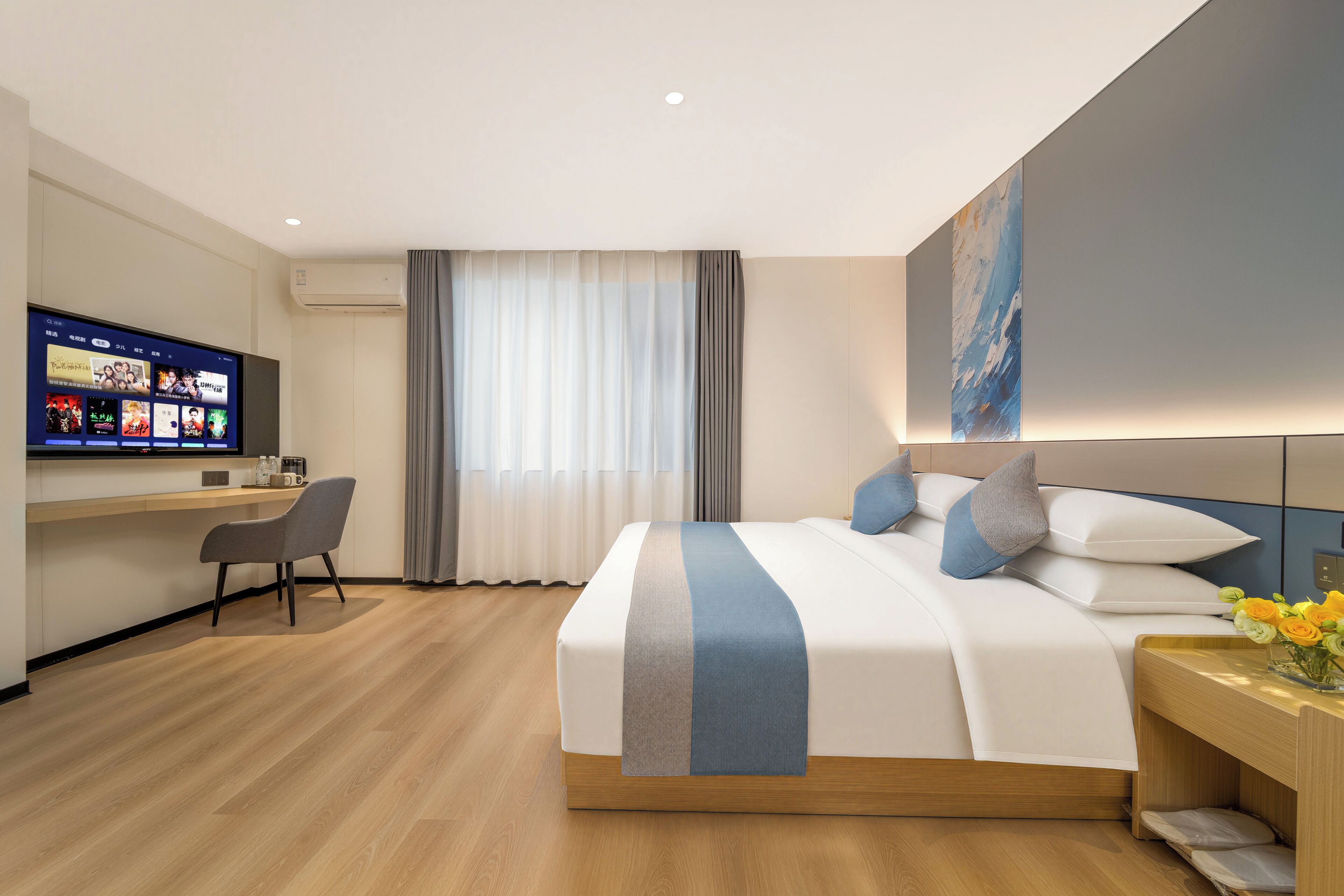 Quarto de hotel com cama, escrivaninha, televisão e janela com cortinas.