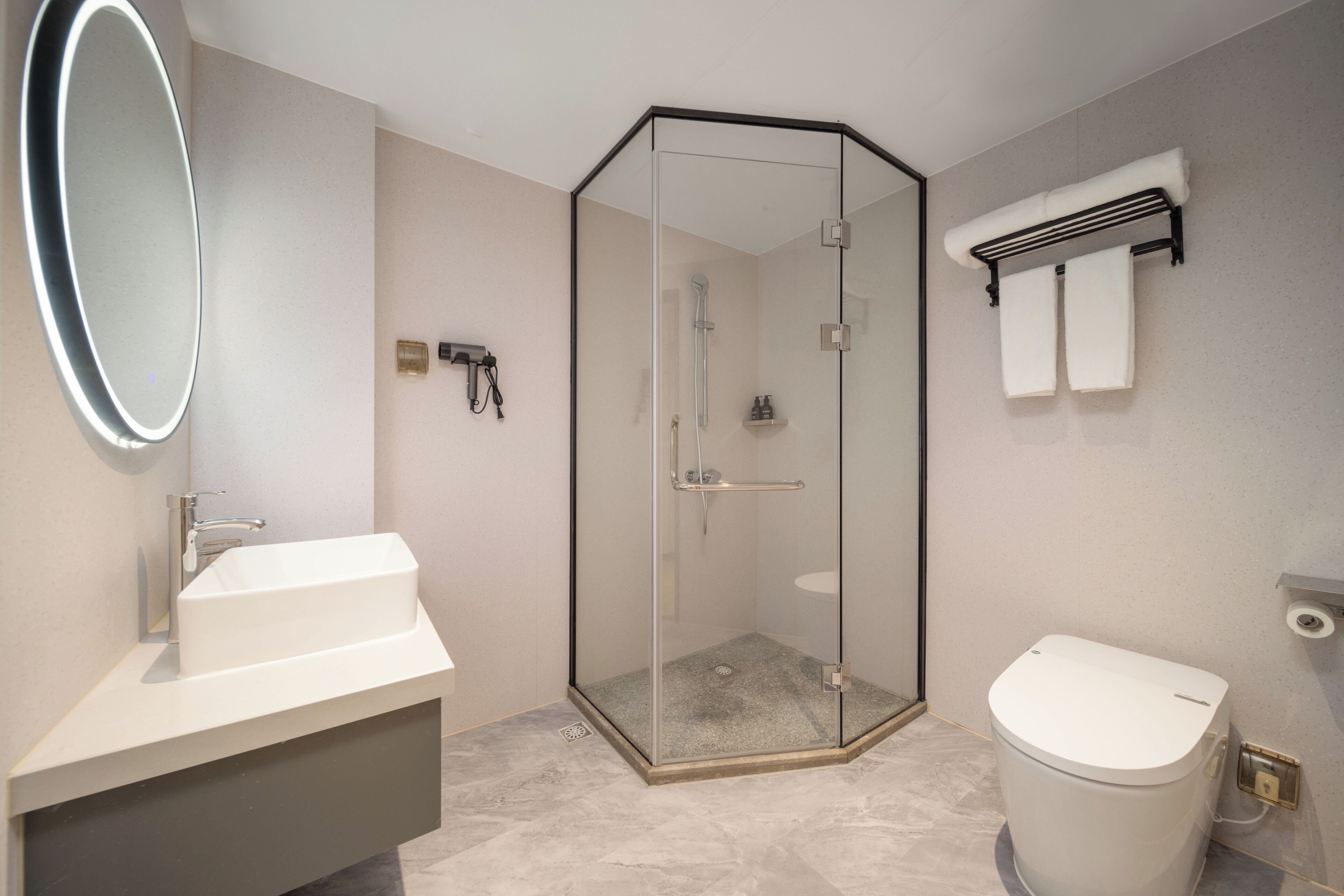 A bathroom with a glass-enclosed shower, a sink, a toilet, a mirror, and a towel rack.