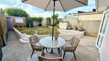 A patio with a round table and chairs, a large umbrella, and a wooden fence in the background.