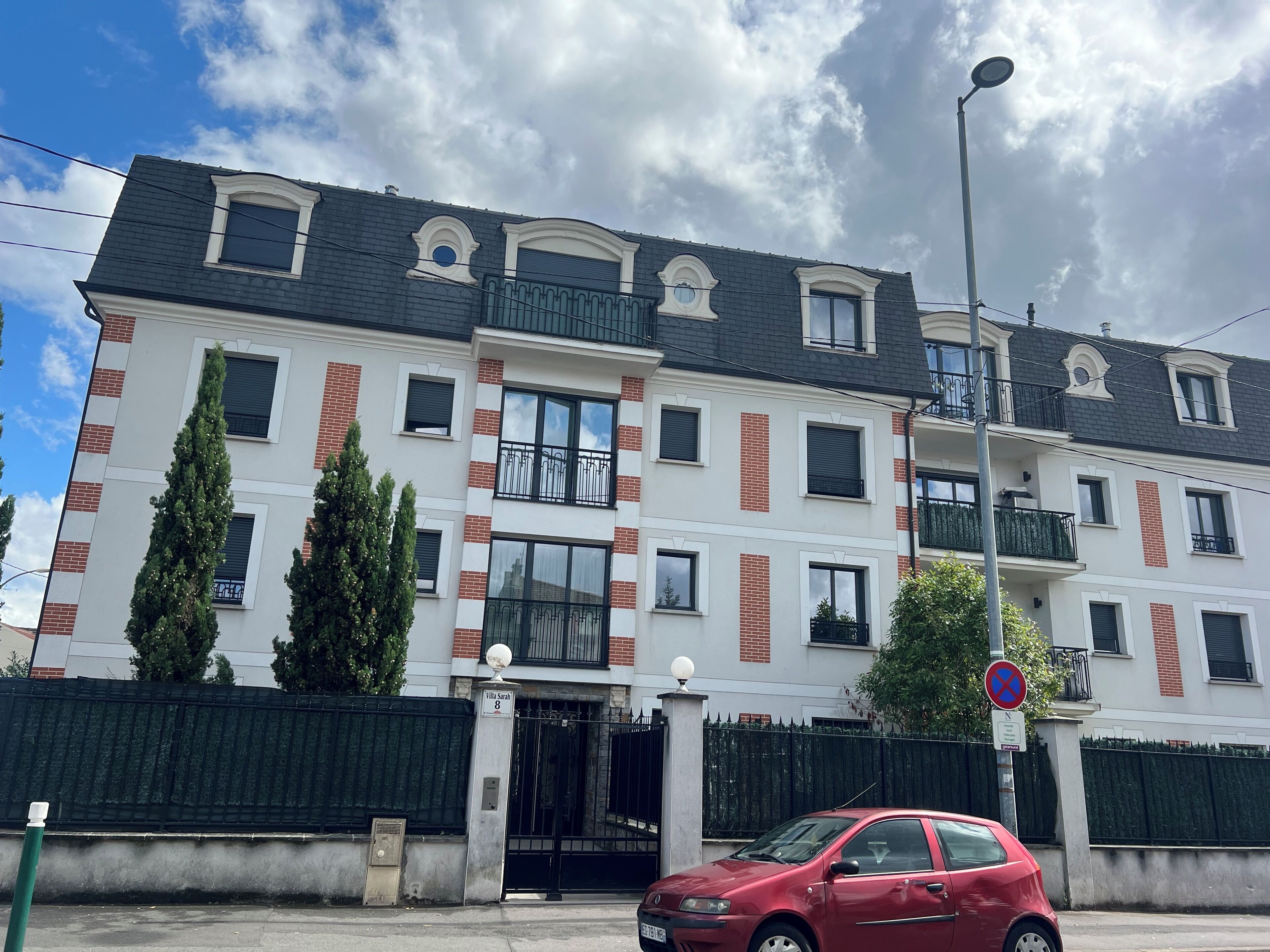 Un immeuble à plusieurs étages, doté d’une entrée fermée par un portail, de balcons et d’un lampadaire.