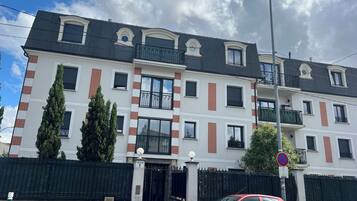 Un immeuble à plusieurs étages, doté d’une entrée fermée par un portail, de balcons et d’un lampadaire.