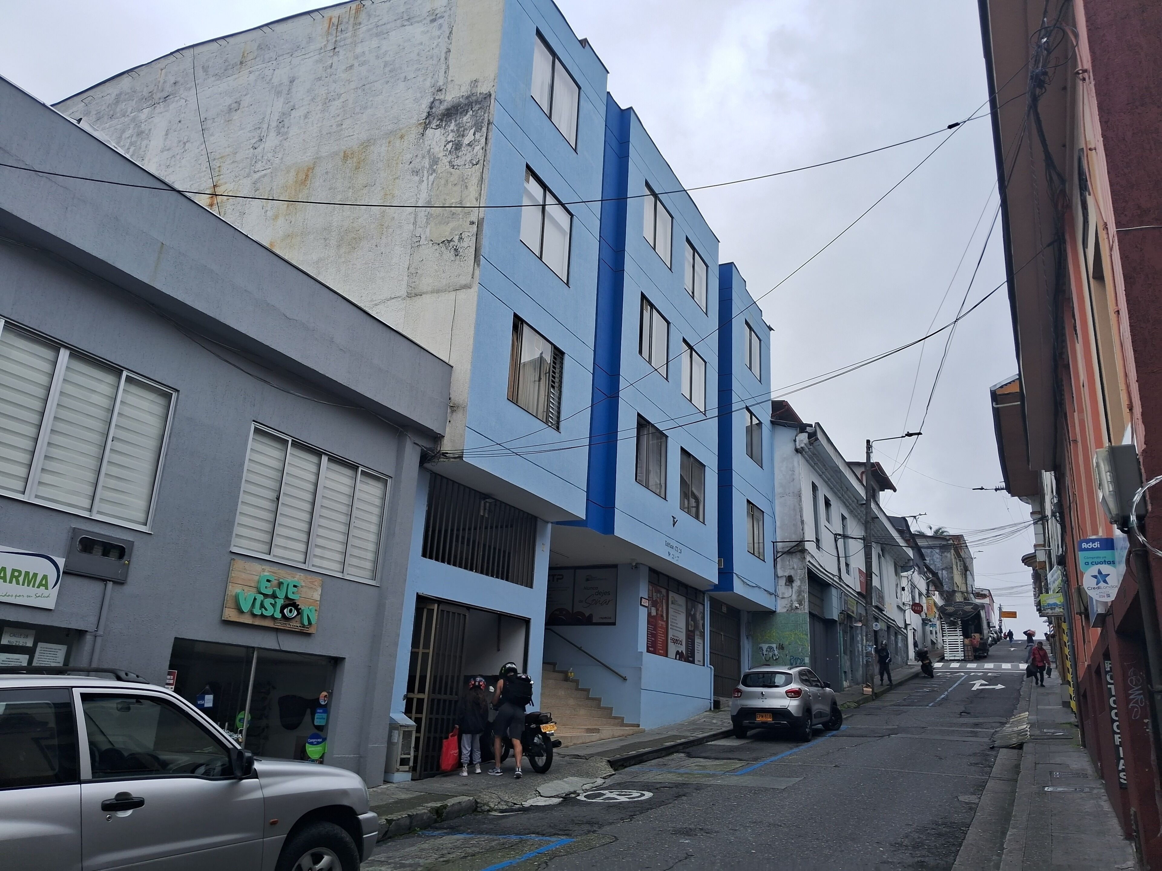 A narrow urban street with buildings, a parked car, and a motorcycle.