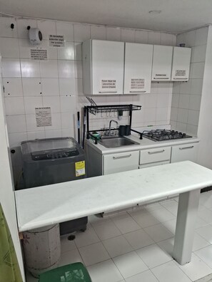 Une cuisine avec des meubles blancs, un évier, une cuisinière à gaz et un plan de travail.