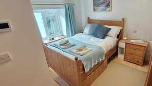 A bedroom with a wooden bed, a bedside table, a nightstand, a window with curtains, and a painting on the wall. - 2 Mins Walk to Beach - Pet-Friendly - Cosy Cottage Llangrannog (Llangrannog)