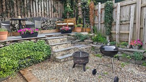 A patio with a stone wall, a wooden bench, a grill, and potted plants. - 2 Mins Walk to Beach - Pet-Friendly - Cosy Cottage Llangrannog (Llangrannog)
