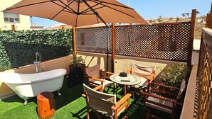 Un patio con una vasca idromassaggio, sedie in legno, un tavolo e un ombrellone.