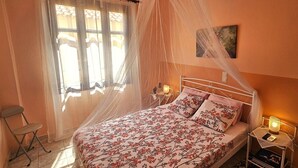 Una camera da letto con un letto, un comodino con una lampada, una sedia, una finestra con tende e un quadro appeso al muro.