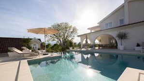 A swimming pool with lounge chairs and umbrellas, a building with arches, and a clear sky. - Luxury villa Speranza with heated saltwater pool (VINJANI DONJI,IMOTSKI)