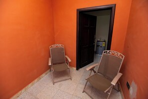 A narrow hallway with two metal chairs, a dark door, and a small trash bin. - Luxury 1 and 2 bedrooms house in nice Braives with cool AC (Braives)