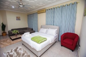 A bedroom with a bed, a red chair, a grey sofa, a ceiling fan, and a wall-mounted air conditioner. - Luxury 1 and 2 bedrooms house in nice Braives with cool AC (Braives)