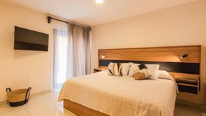 A hotel room with a large bed, a flat-screen TV mounted on the wall, a wooden headboard, and a window with curtains. - Casa Lily  (San Cristóbal de las Casas)