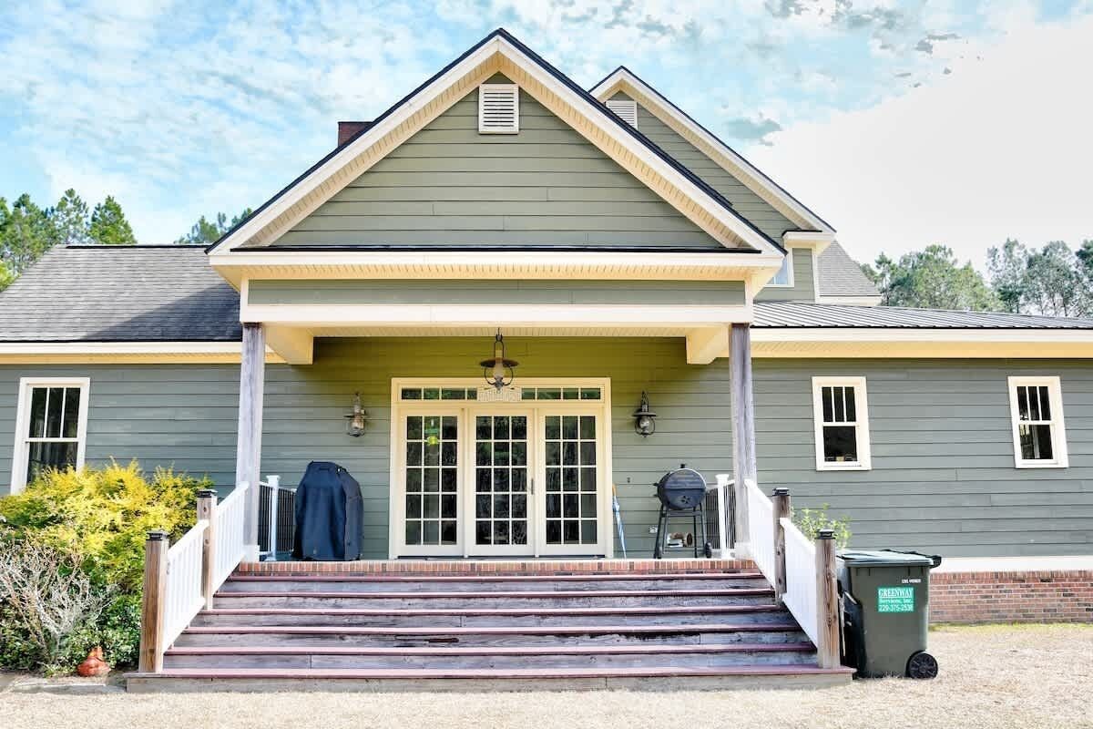 A two-story house with a front porch, a garage door, and a trash bin.