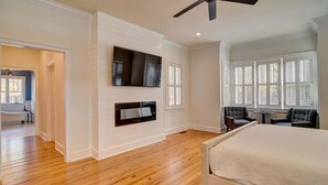 A bedroom with a bed, a ceiling fan, a TV mounted on the wall, and a window with blinds.