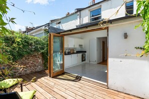 Eine moderne Küche mit weißen Schränken und einer schwarzen Arbeitsplatte, einer Holzterrasse und einer Glastür, die zu einem Raum führt.