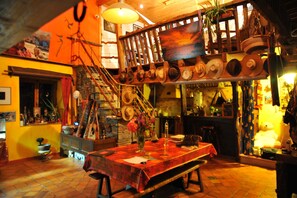 A dining area with a table set for two, a staircase, and a variety of hats displayed on the wall. - Bed and Breakfast 'Chambre D'hôtes Erziwezh' with Private Garden and Wi-Fi (Sainte-Marie)