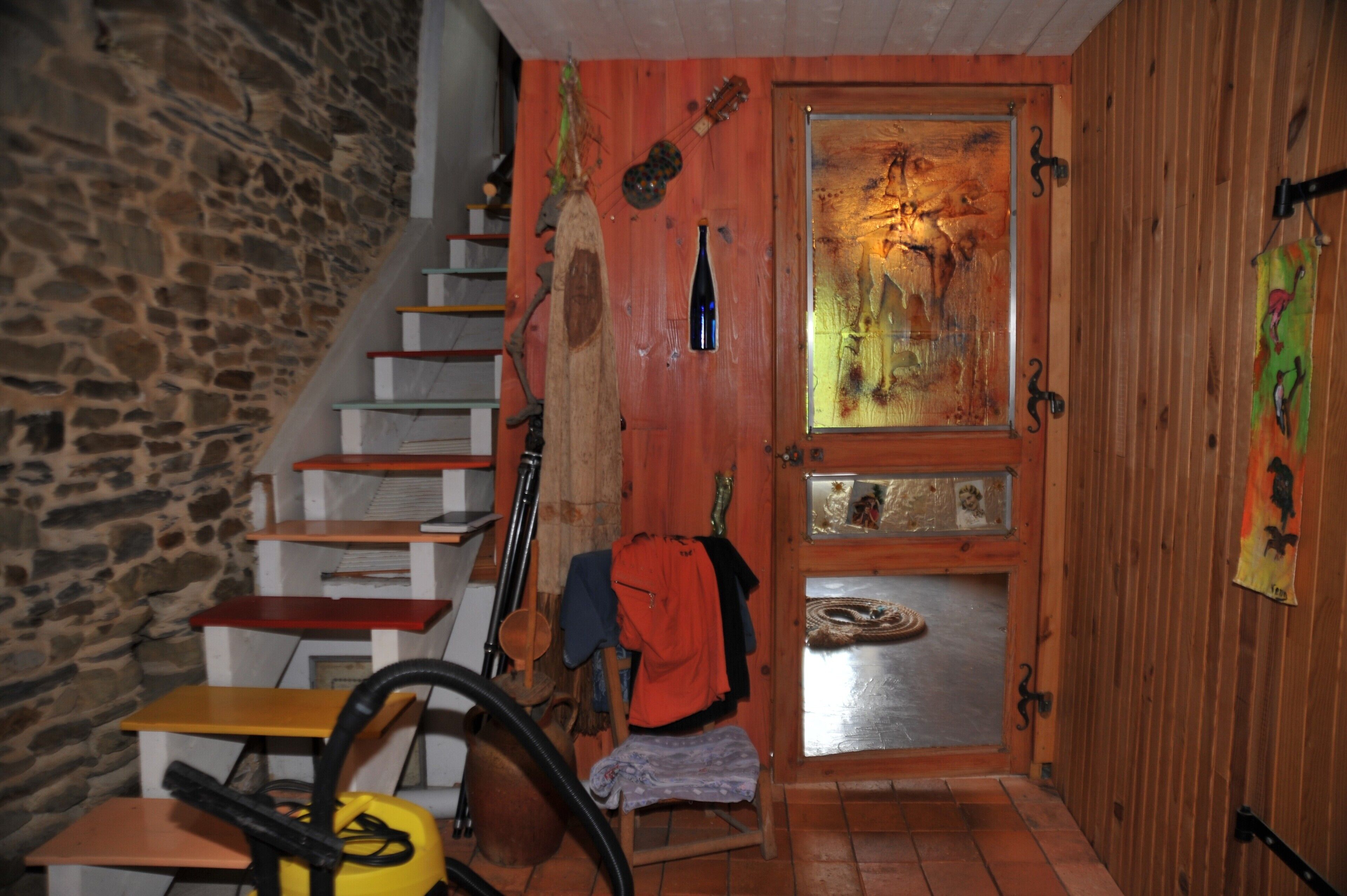 A rustic interior with a wooden staircase, a door with artwork, and a stone wall.