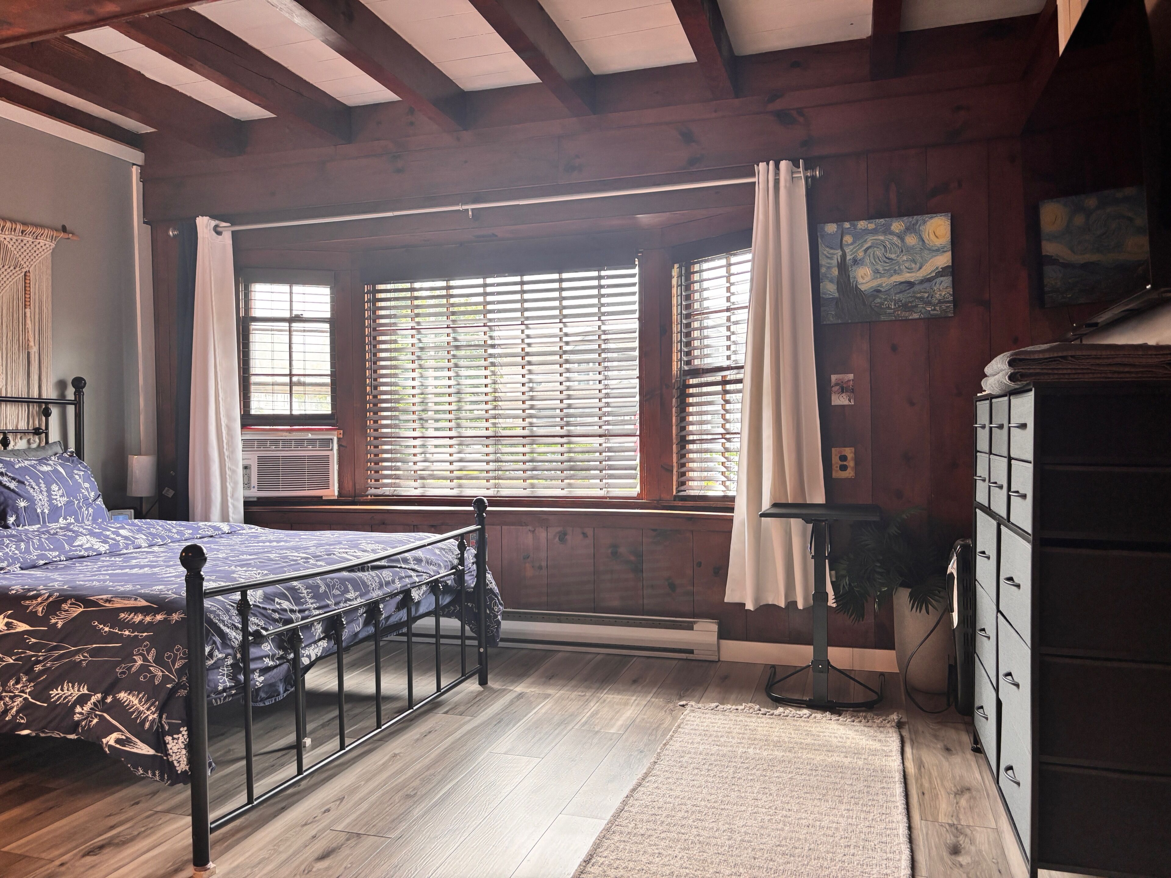 A bedroom with a bed, a dresser, a window with blinds, and a painting on the wall.