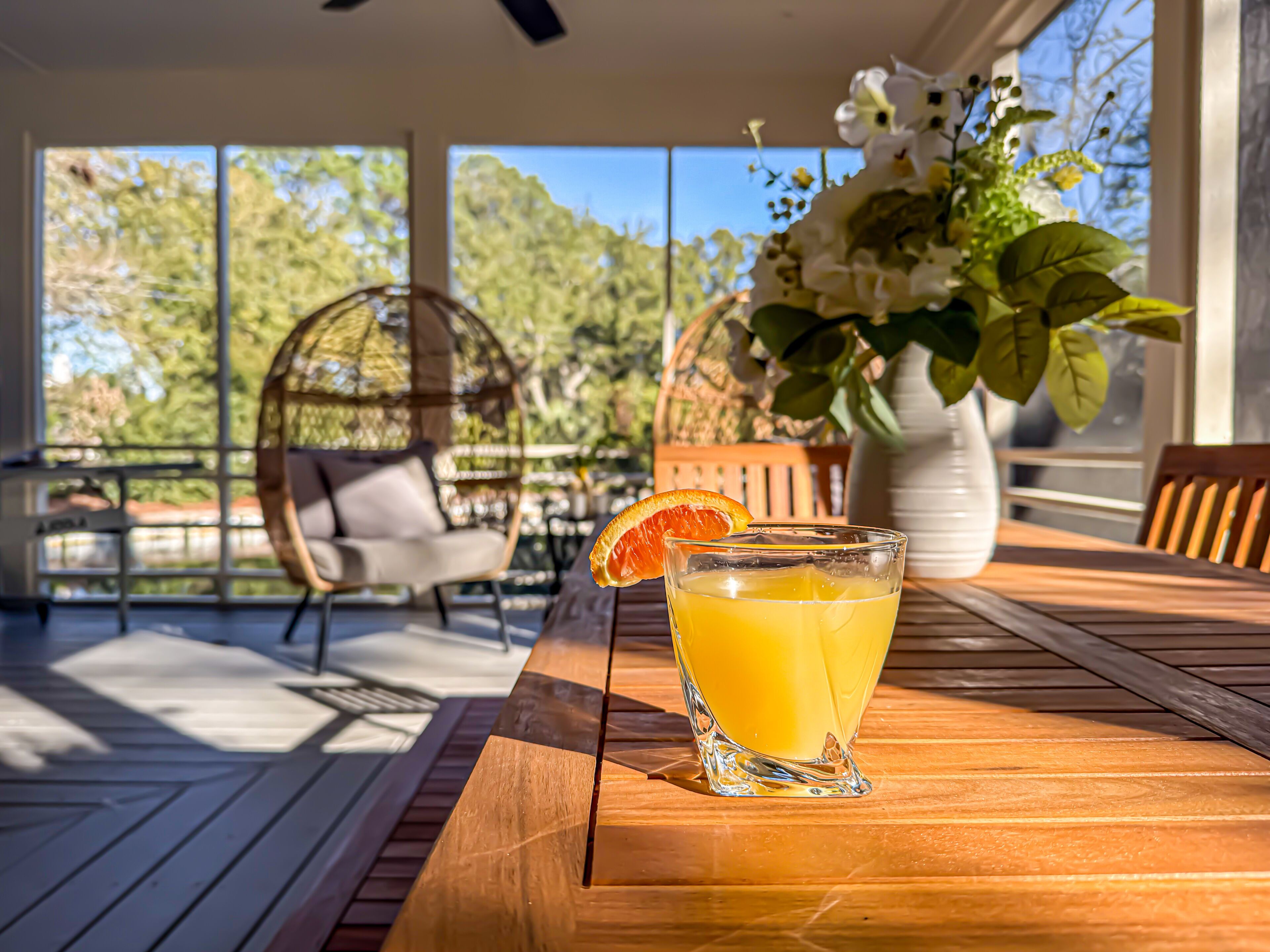 Ein Glas Orangensaft auf einem Holztisch, im Hintergrund ein Stuhl und ein Hängesessel.