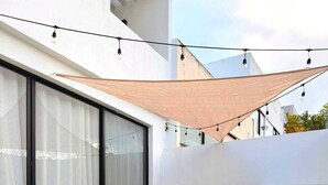 Area piscina esterna moderna con acqua cristallina, due lettini, una ghirlanda di luci e un'ampia finestra con tende leggere.