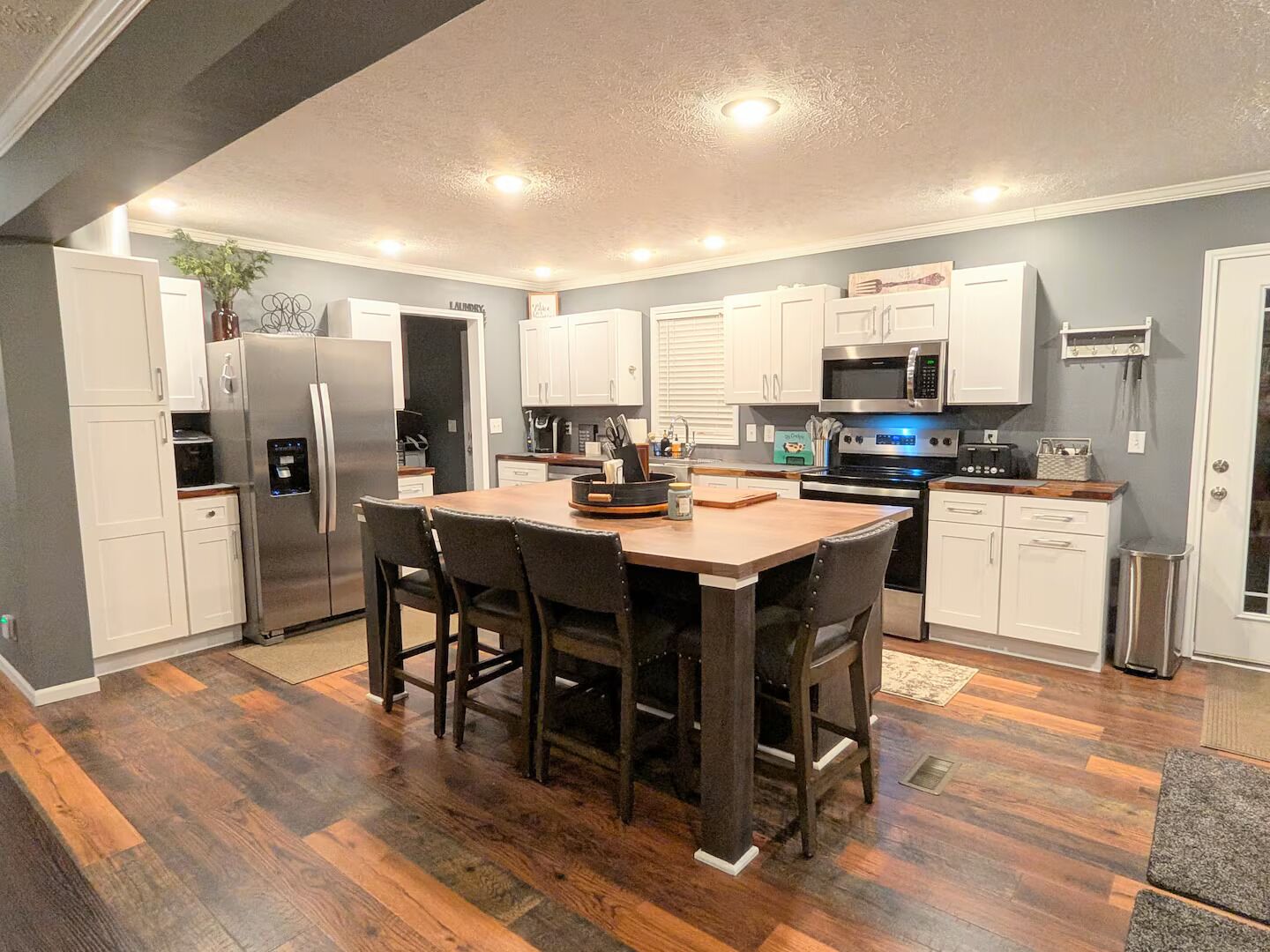 A modern kitchen with white cabinets, a stainless steel refrigerator, a microwave, and a dining area with a wooden table and chairs.