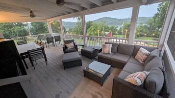 A covered outdoor deck with seating, a table, and a view of a green landscape.