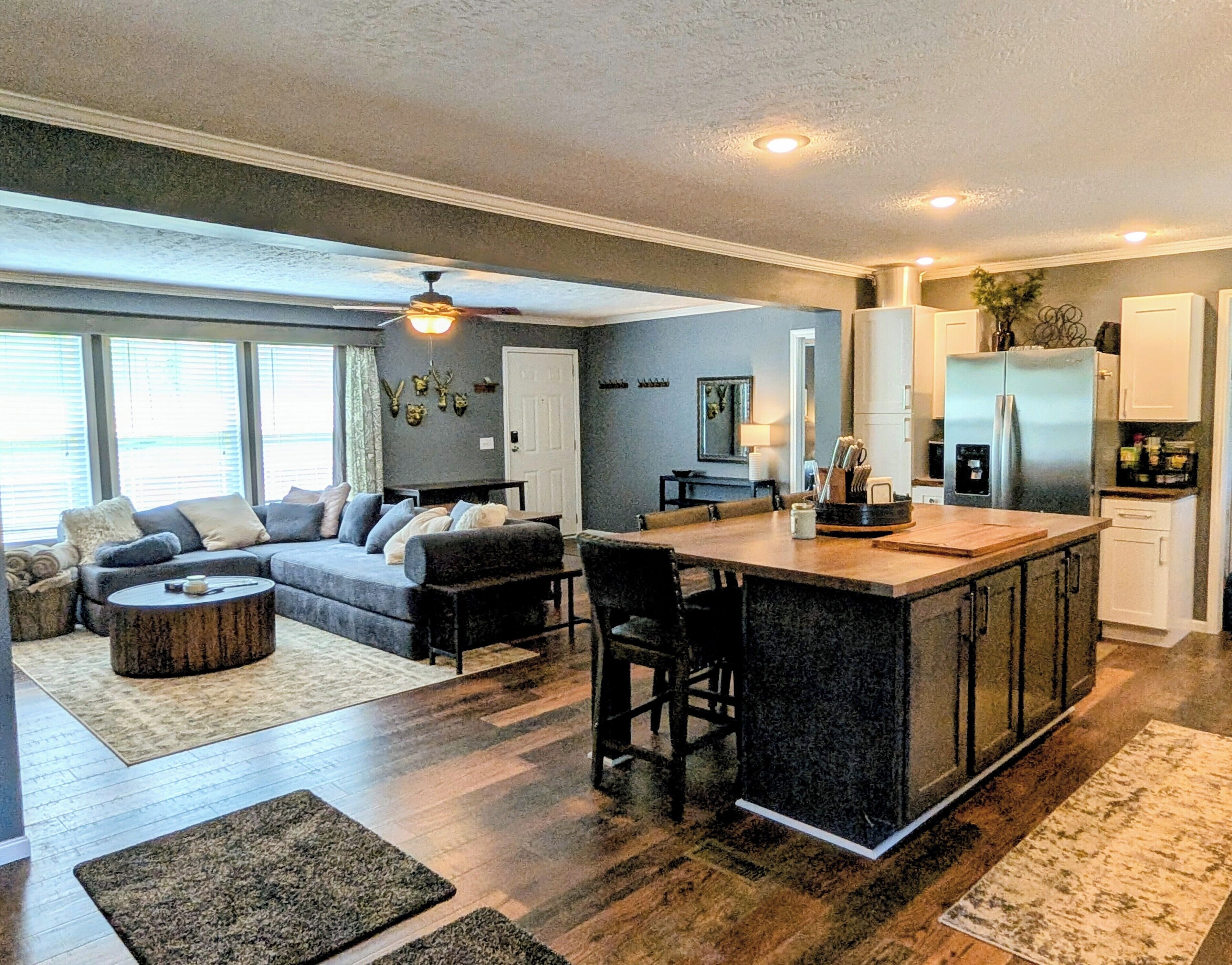 A modern kitchen with a central island, a dining area with a sofa and chairs, and a living room with a large couch and a fireplace.