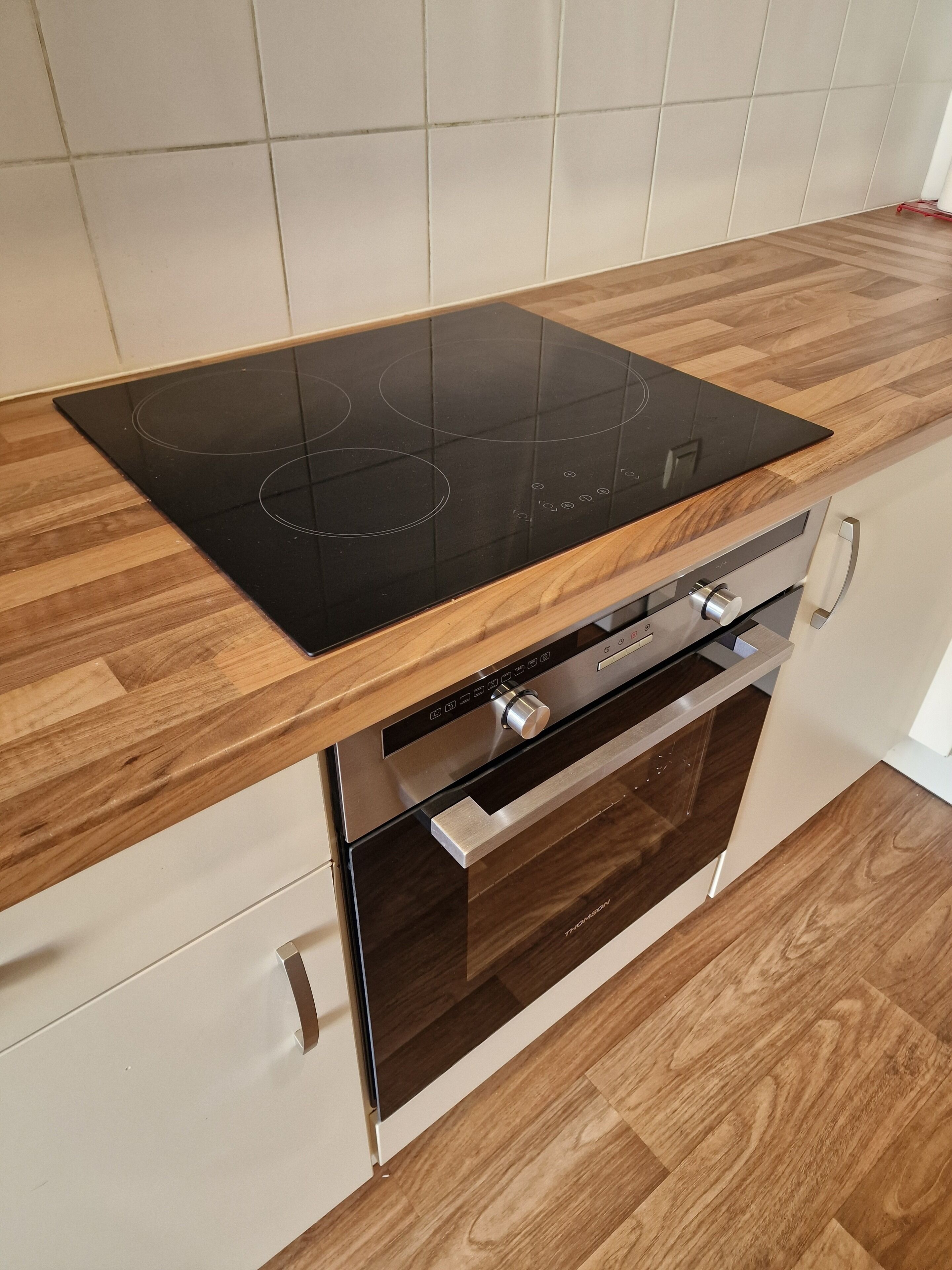 A kitchen with a black induction cooktop, wooden countertop, stainless steel appliances, and a white tiled backsplash.