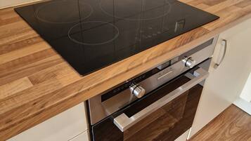 A kitchen with a black induction cooktop, wooden countertop, stainless steel appliances, and a white tiled backsplash.