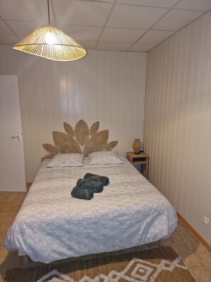 A bedroom with a bed, a hanging light fixture, a nightstand, and a door. - A single-story house with a warm and welcoming atmosphere, located in the heart of the village (Lantriac)