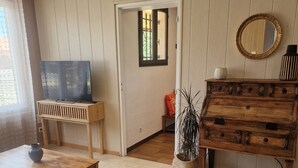 Olohuoneessa on televisio puisen jalustan päällä, puinen lipasto, peili ja ruukussa oleva huonekasvi.