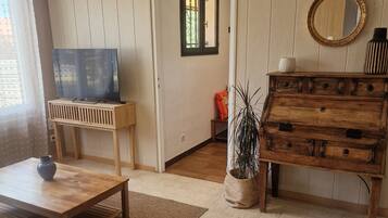 A living room with a television on a wooden stand, a wooden dresser, a mirror, and a potted plant.