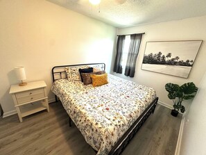 A bedroom with a bed, bedside table, lamp, curtains, and a wall-mounted plant. - Home in Panama City - Seahorse Oasis (Panama City)